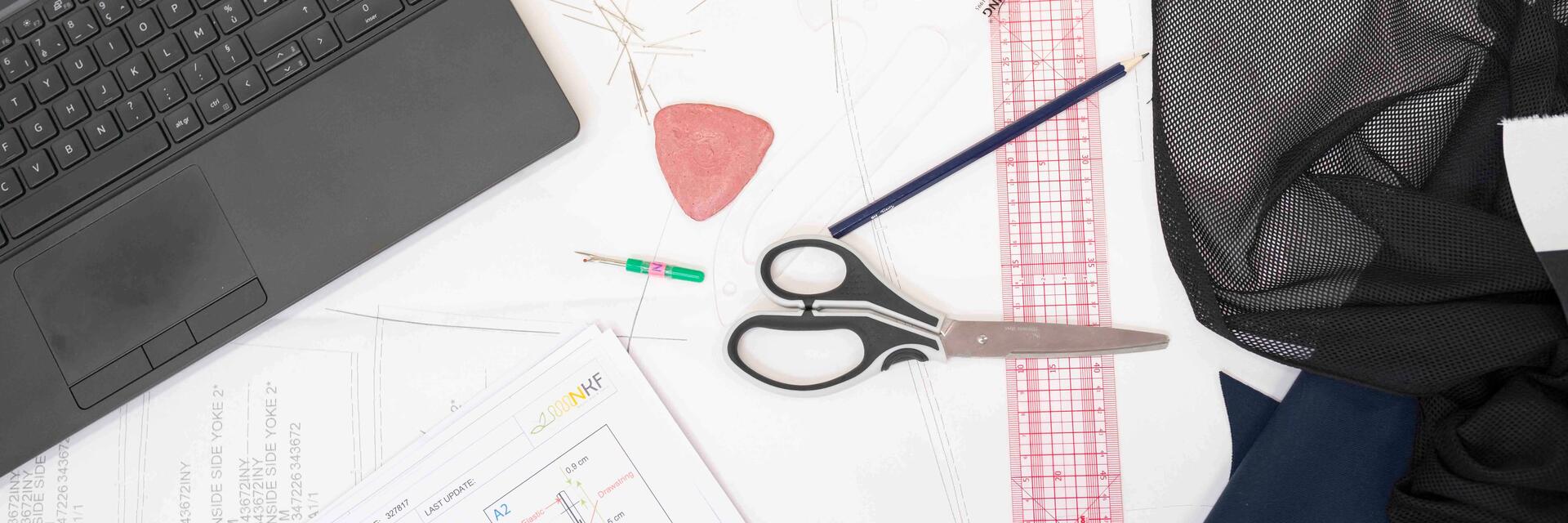 Looking down at table that has placed on top clothing design items; pencil. eraser, ruler, scissors, fabris