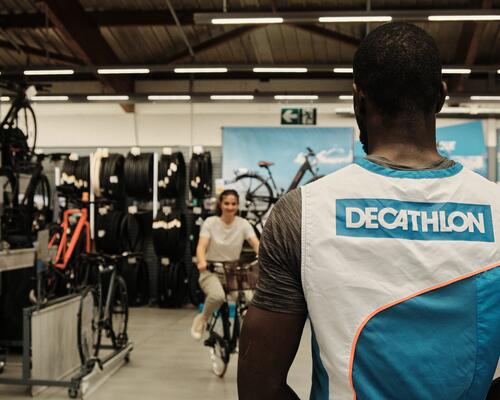 na imagem vemos um colaborador Decathlon a auxiliar uma pessoa na area das bicicletas