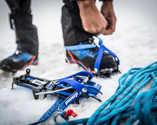 Alpinista a colocar crampons 