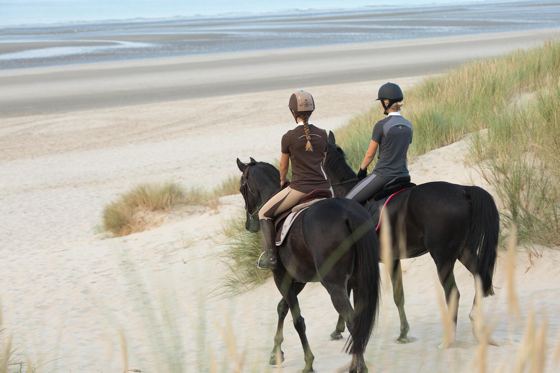 Deux cavalière en train de traverser les dunes pour aller à la plage à cheval