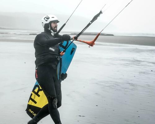 mężczyzna idący z deską kitesurfingową i uprzężą 