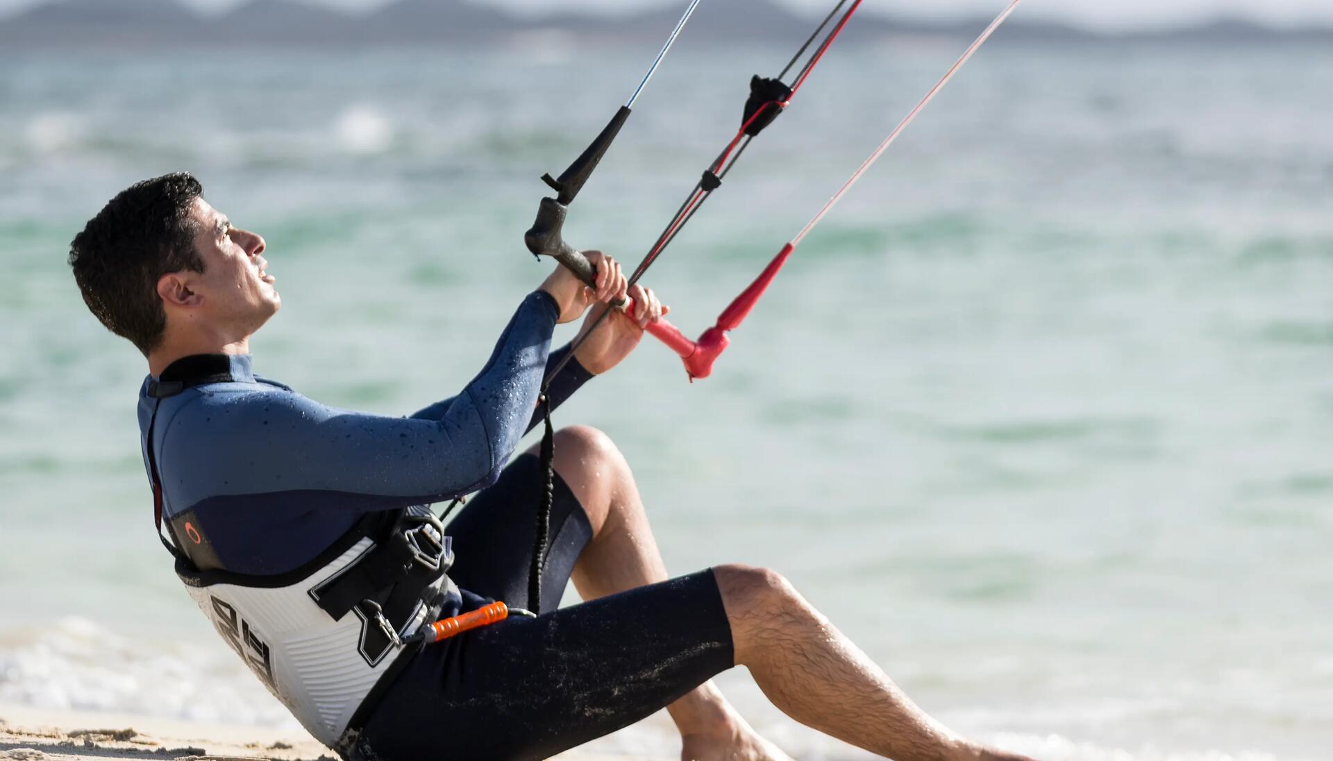 mężczyzna przypięty do latawca kitesurfingowego na plaży