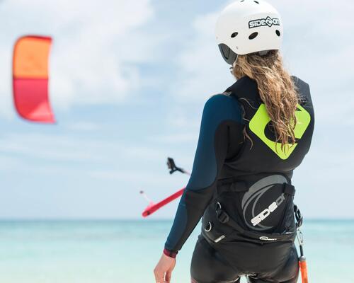 kobieta w kasku i piance surfingowej przypięta do latawca kitesurfingowego