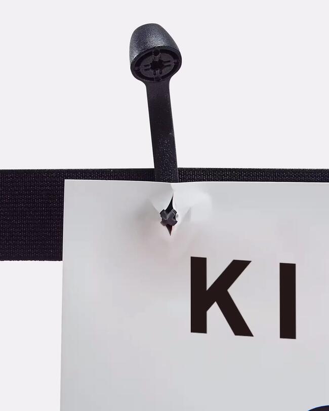 Schwarzes Startnummerband mit Klettverschluss, hält weißen Zettel. Schwarze Kunststoffbefestigung durchdringt Papier.
