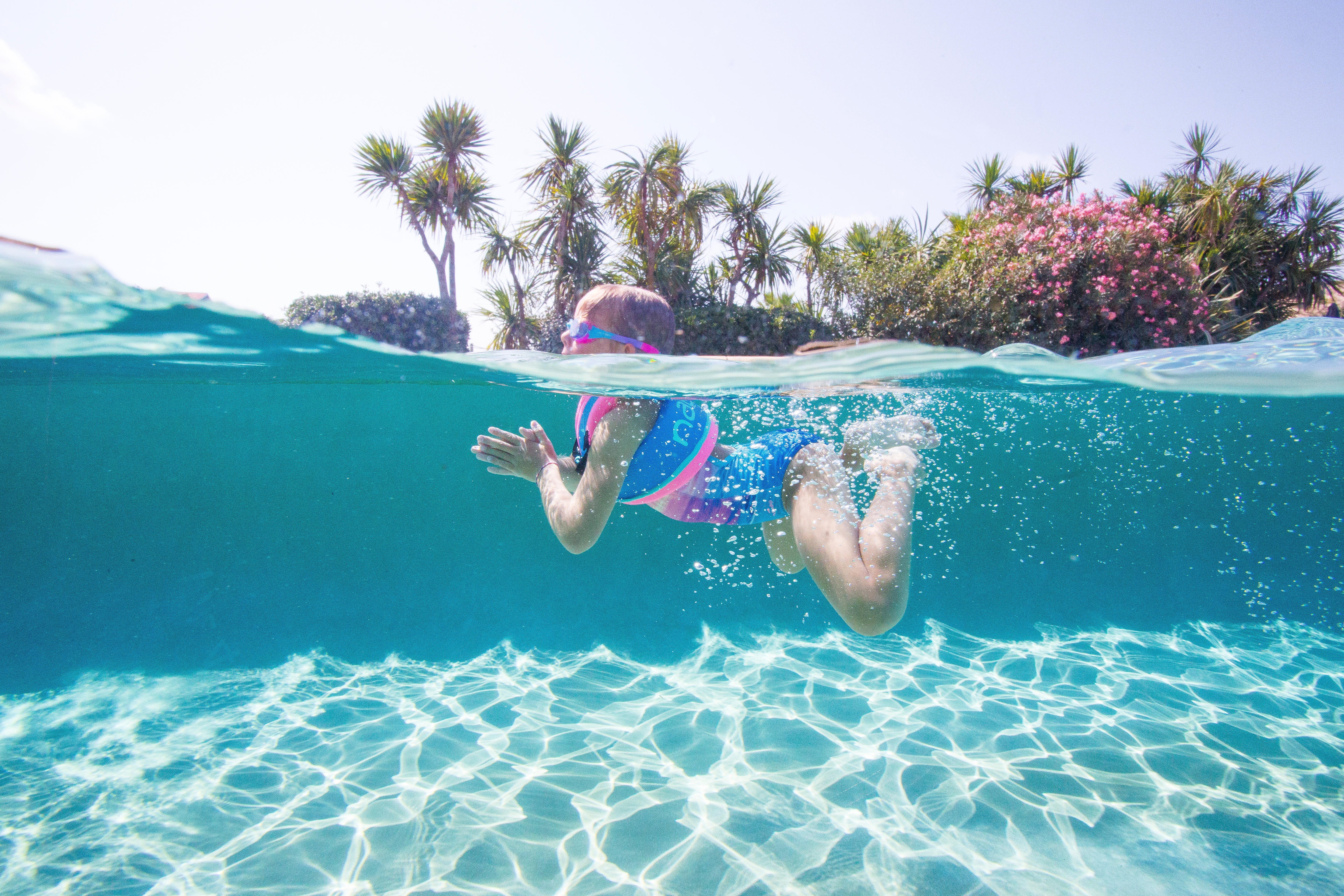 Toddler wearing a swim vest while swimming in clear shallow water.