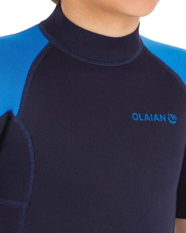  Nahaufnahme des Halsbereichs eines dunkelblauen Wetsuits mit blauen Ärmeln und dem "OLAÏAN"-Logo auf der Brust, was auf Komfort und Reibungsfreiheit hinweist.