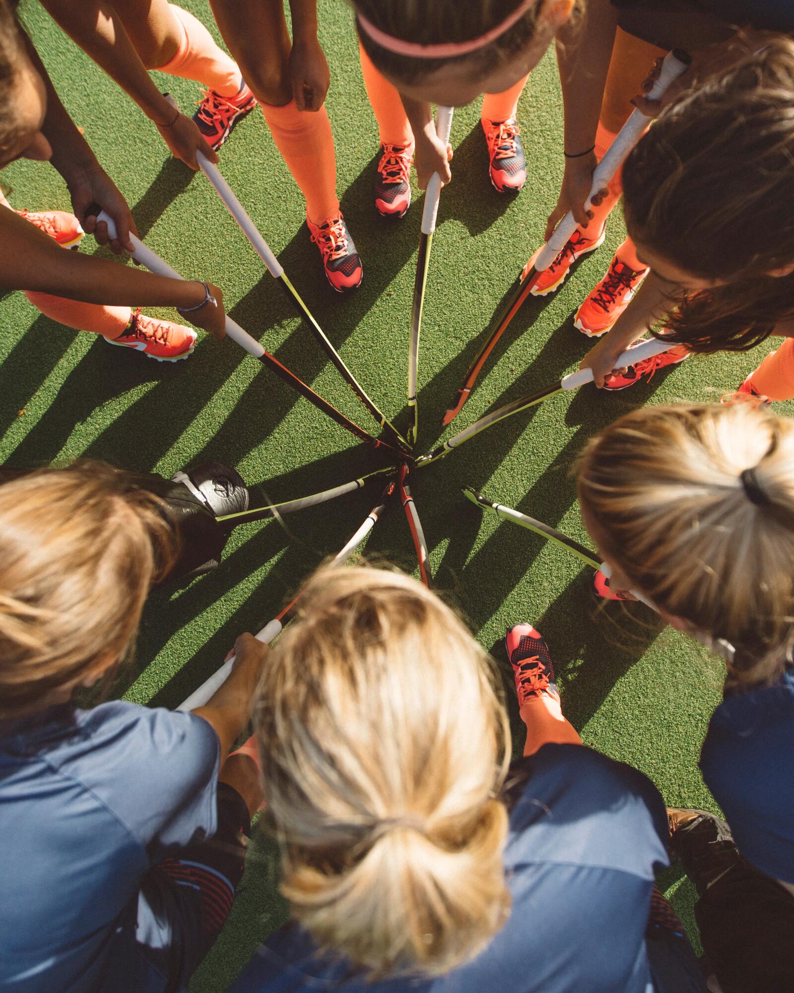 Frauen mit Hockeyschläger von oben, wie sie ihre Schläger in die Mitte halten.