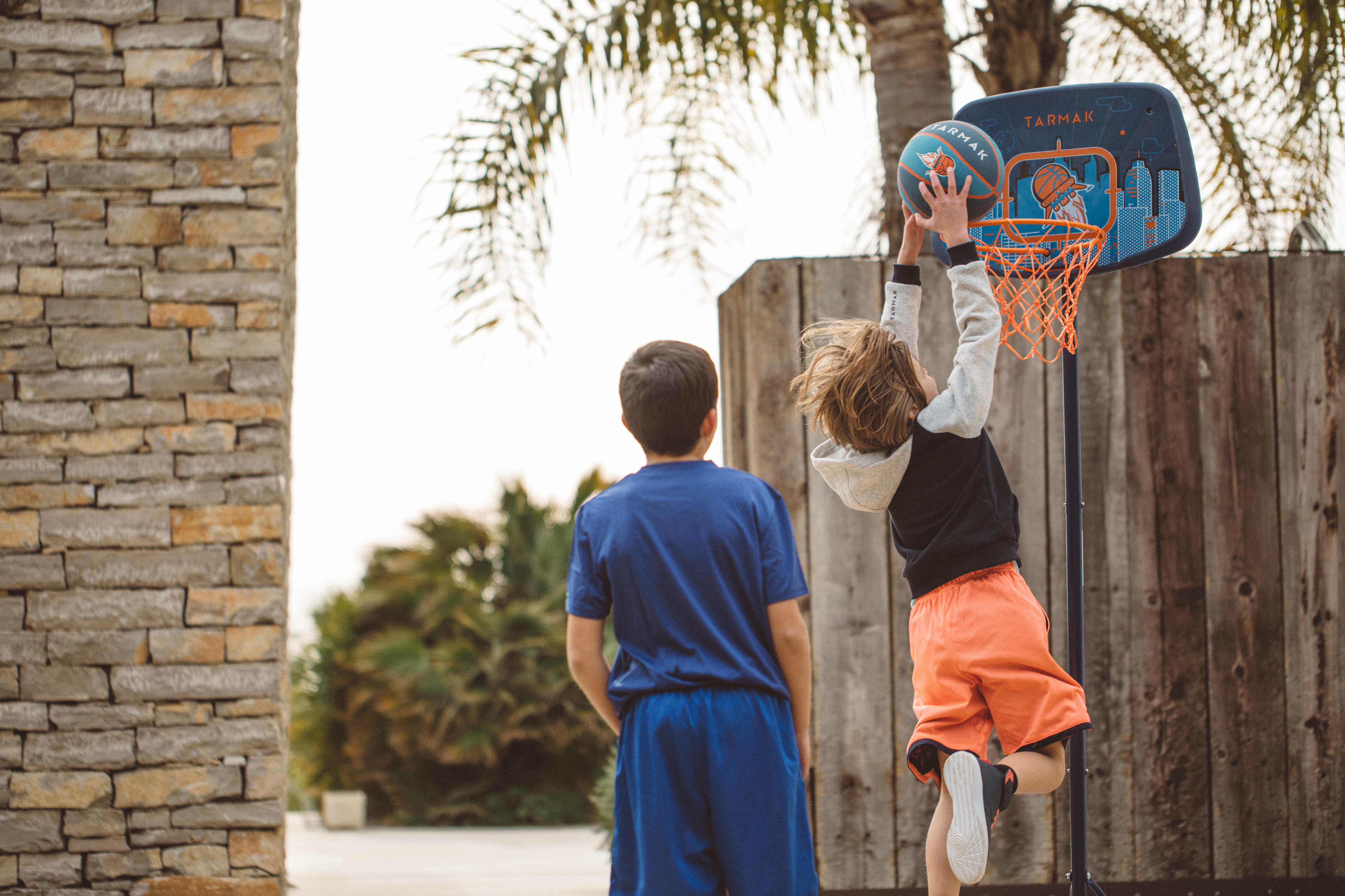 Boy shooting basketball into portable hoop, another boy watching