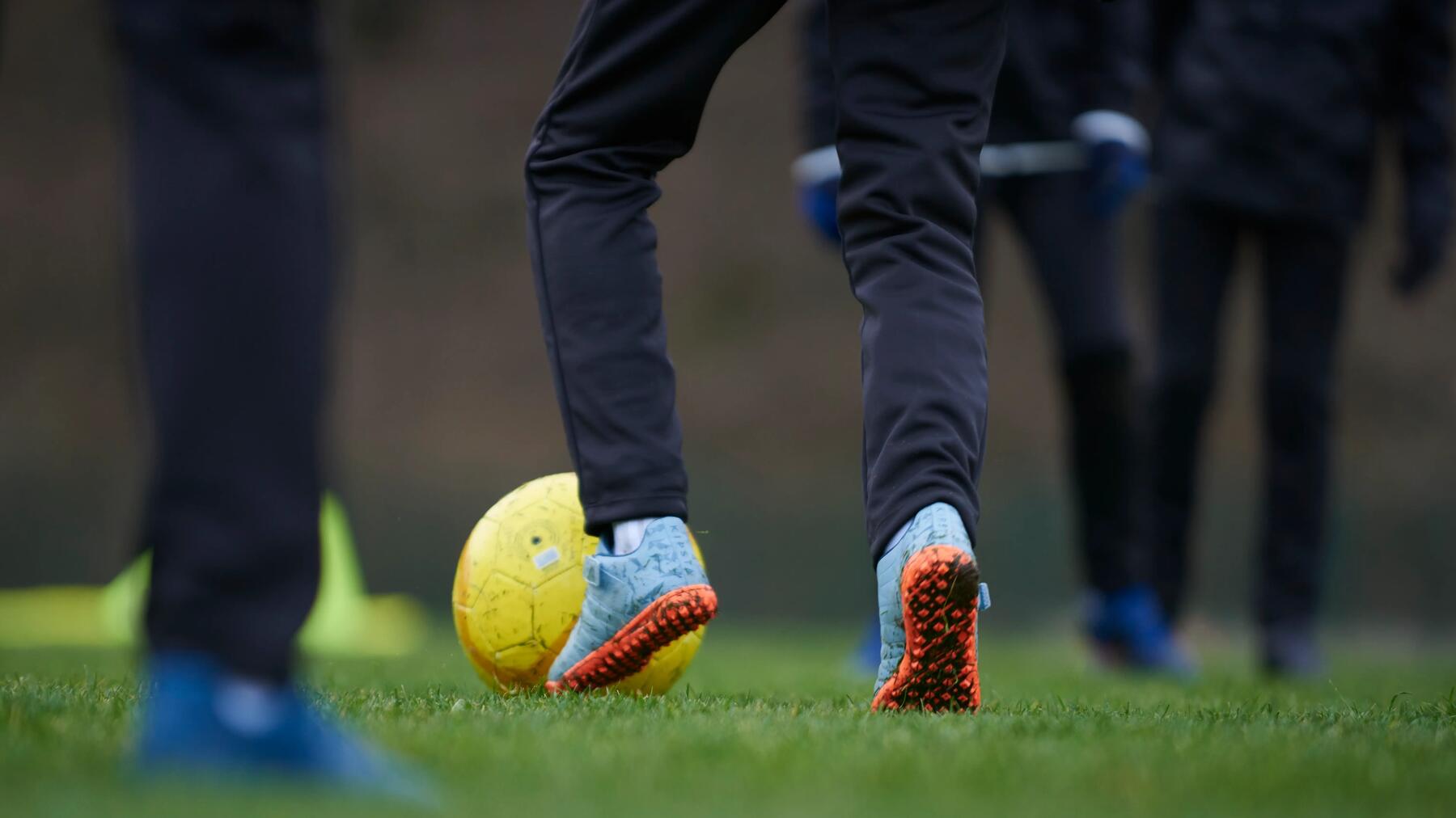 persoon met een voetbal aan zijn voeten. je ziet alleen de onderbenen en de voetbal en het voetbalveld
