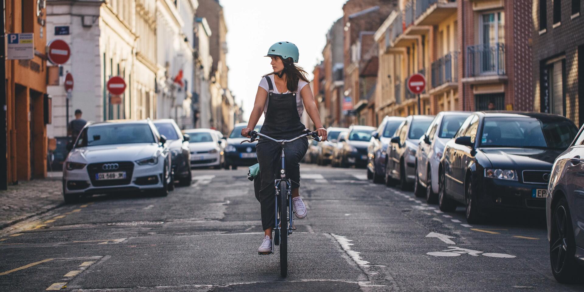 kobieta w kasku rowerowym jadąca na rowerze miejskim ulicą 