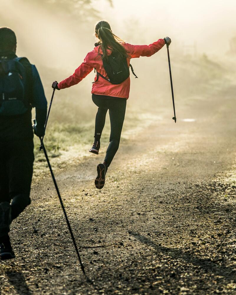 Eine Frau springt glücklich im Wald mit ihren Nordic Walking Stöcken in die Luft.