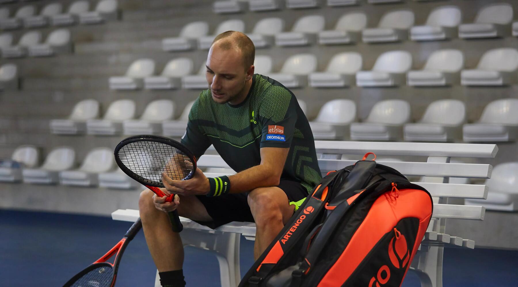 Tennisspieler sitzt im Stadion auf der Spielerbank neben einer Tennistasche der Marke Artengo