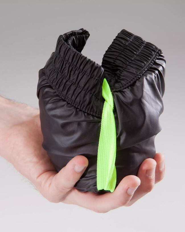 Schwarzer Stoffbeutel mit neon-grünem Band, elastische Ränder, knitterige Textur, von Hand gehalten.