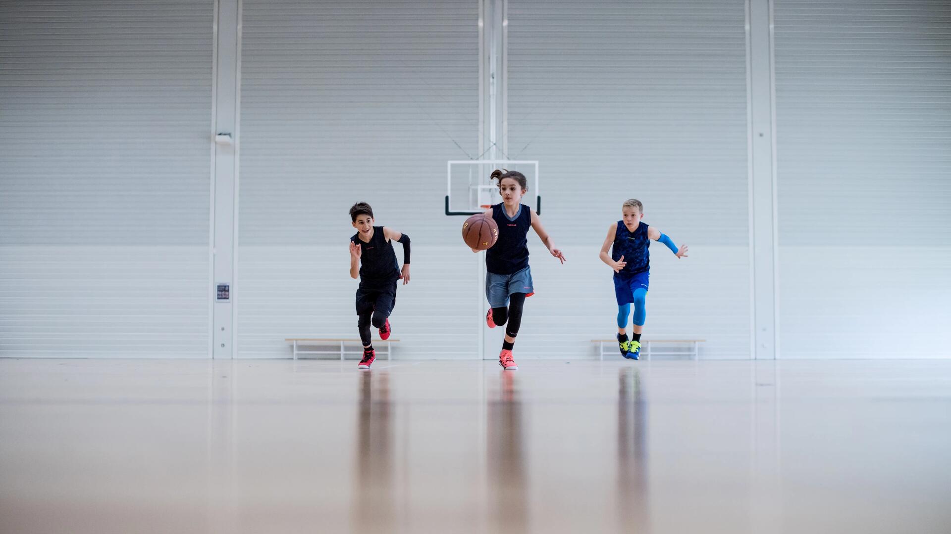 3 jeunes enfants qui pratique le basketball dans un gymnase