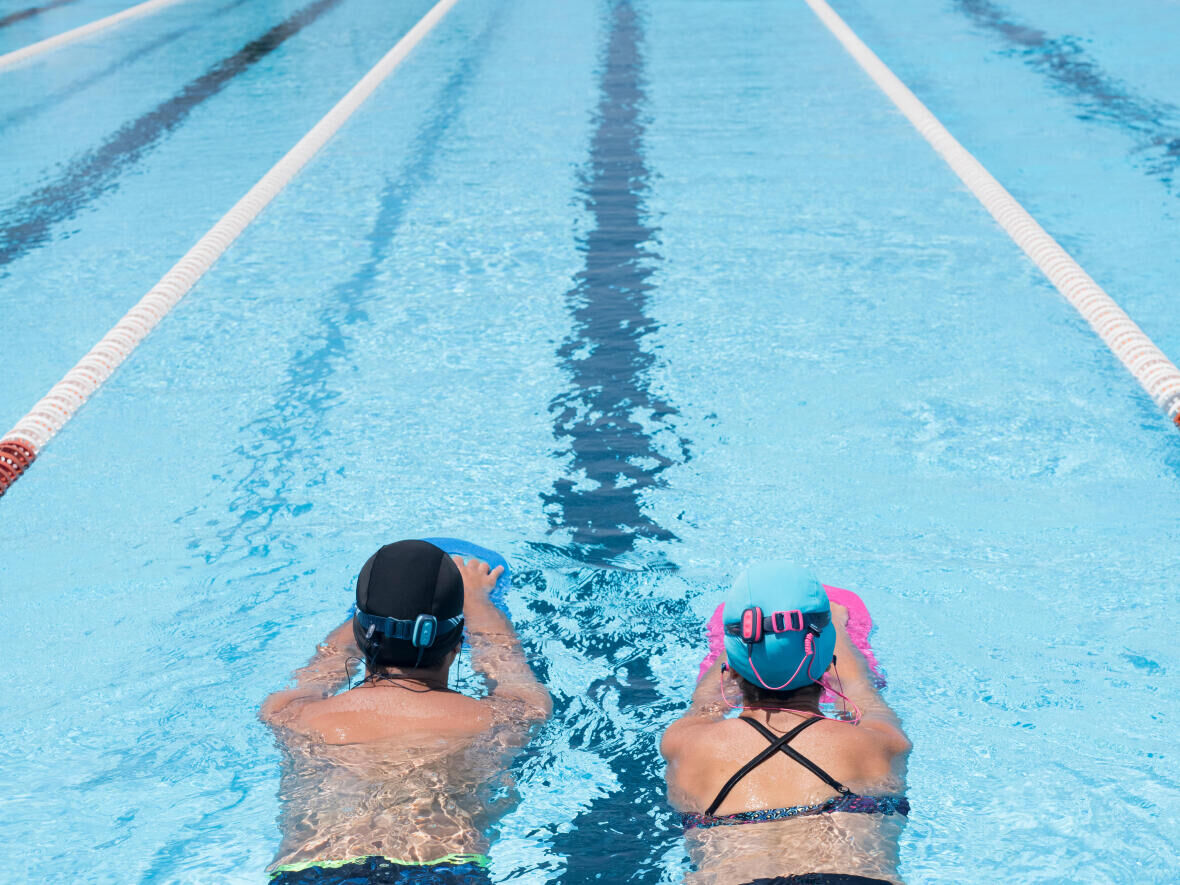 Une nageuse et un nageur en train de nager avec des planches dans une ligne de piscine publique