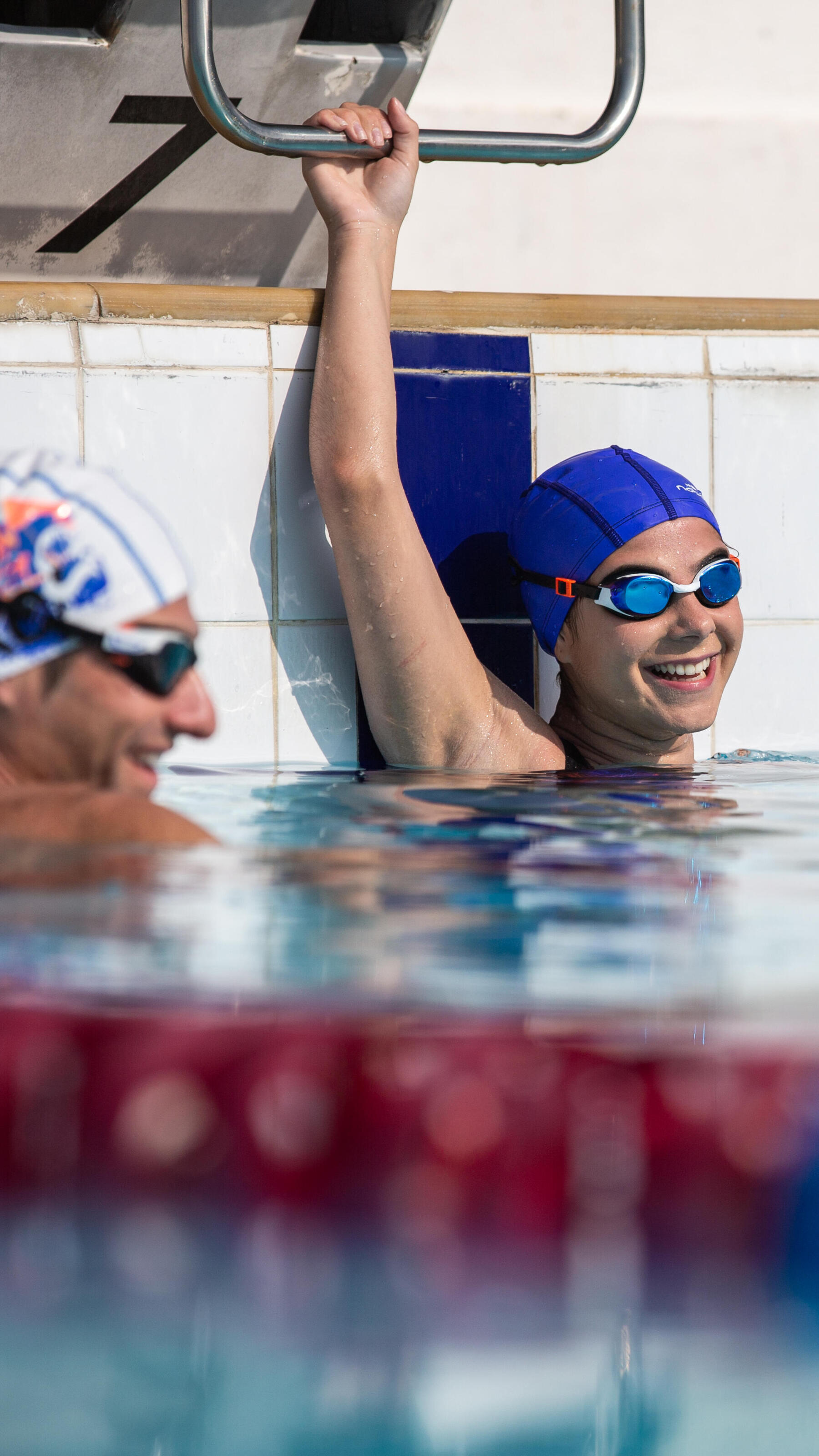Une nageuse et un nageur dans l'eau discutant et souriant pendant une pause lors d'un entraînement en bassin