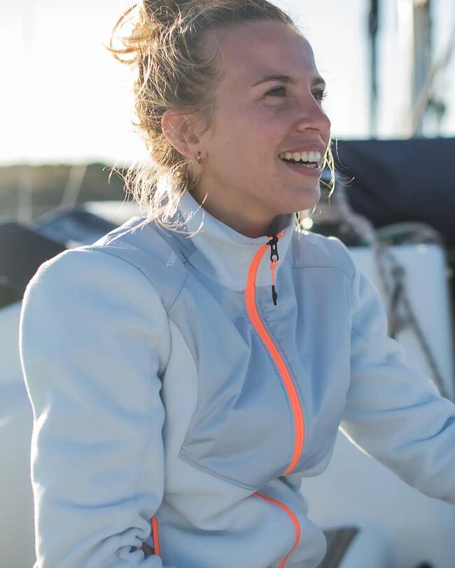 Frau in heller Jacke lächelt; Hintergrund mit Boot und sonnigem Himmel; helle Farben, weiche Texturen.