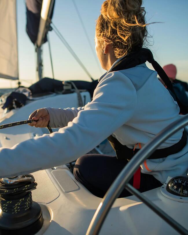 Person steuert weißes Segelboot auf blauem Ozean bei Sonnenuntergang, Wind im Segel, klare Himmel, dynamische Wellen.