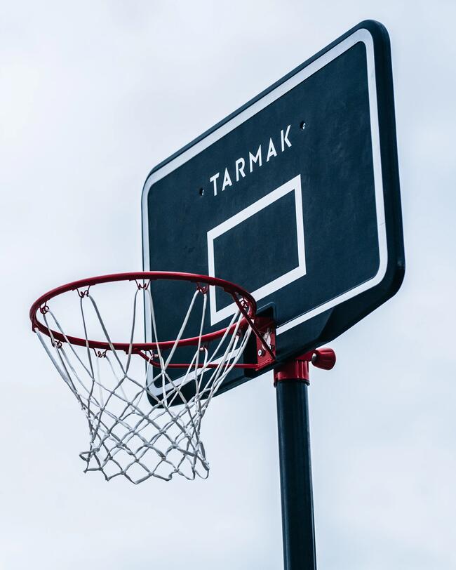 Schwarzes Basketballbrett mit weißem Rand, rotem Ring und Netz vor grauem Himmel.