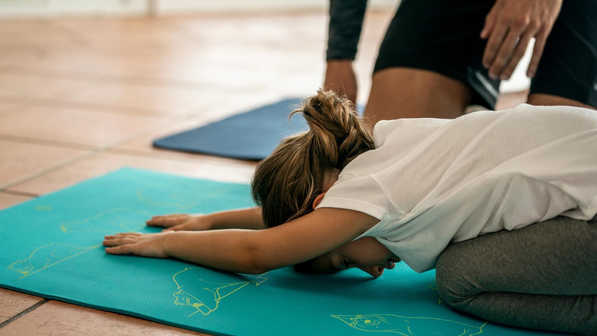 Une petite fille qui fait la position de l'enfant sur un tapis de yoga
