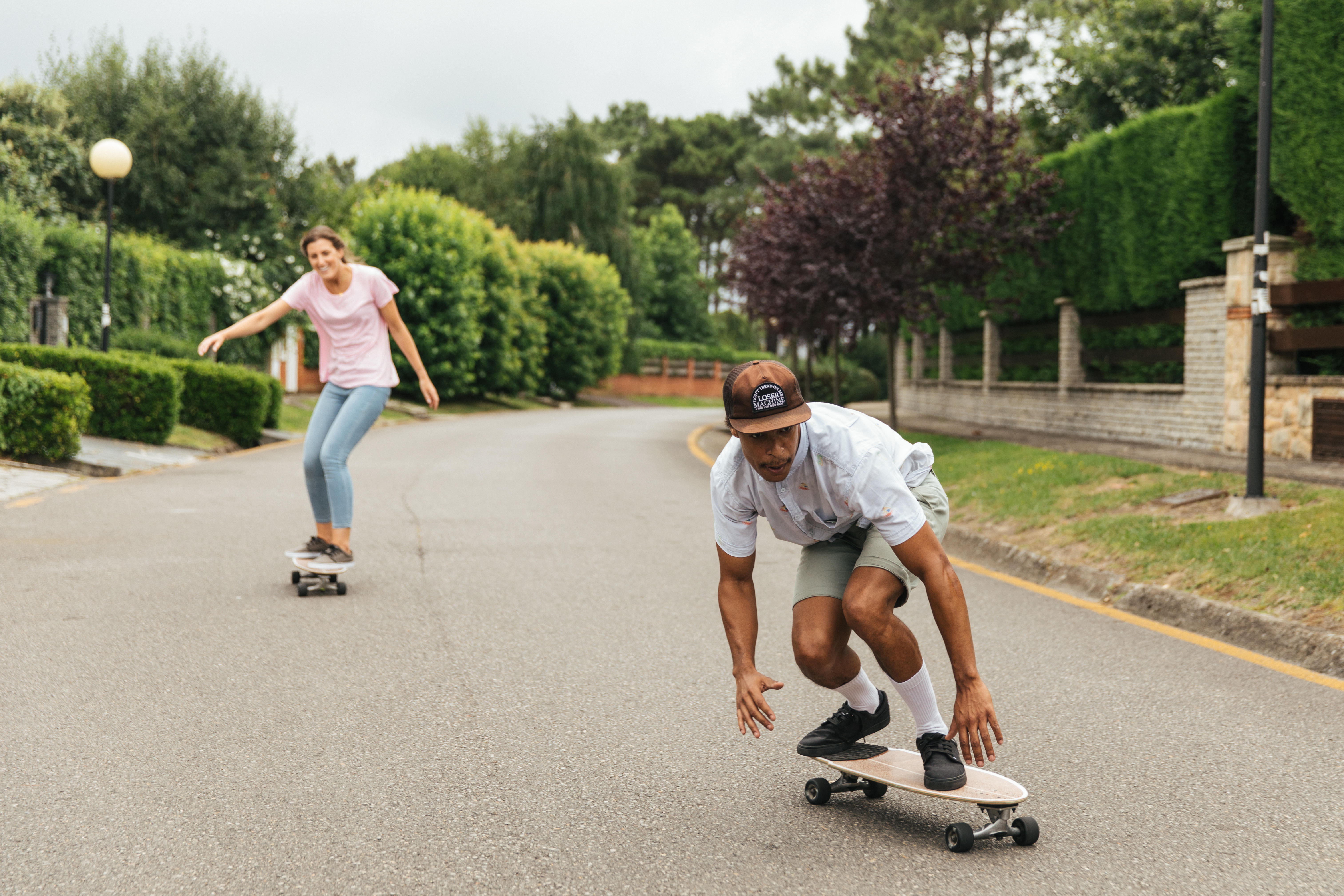 Man crouching low on a longboard as a woman skates behind him