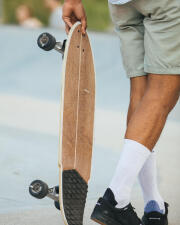 Muž drží v ruce surfskate, má bílé ponožky a černé boty oxelo