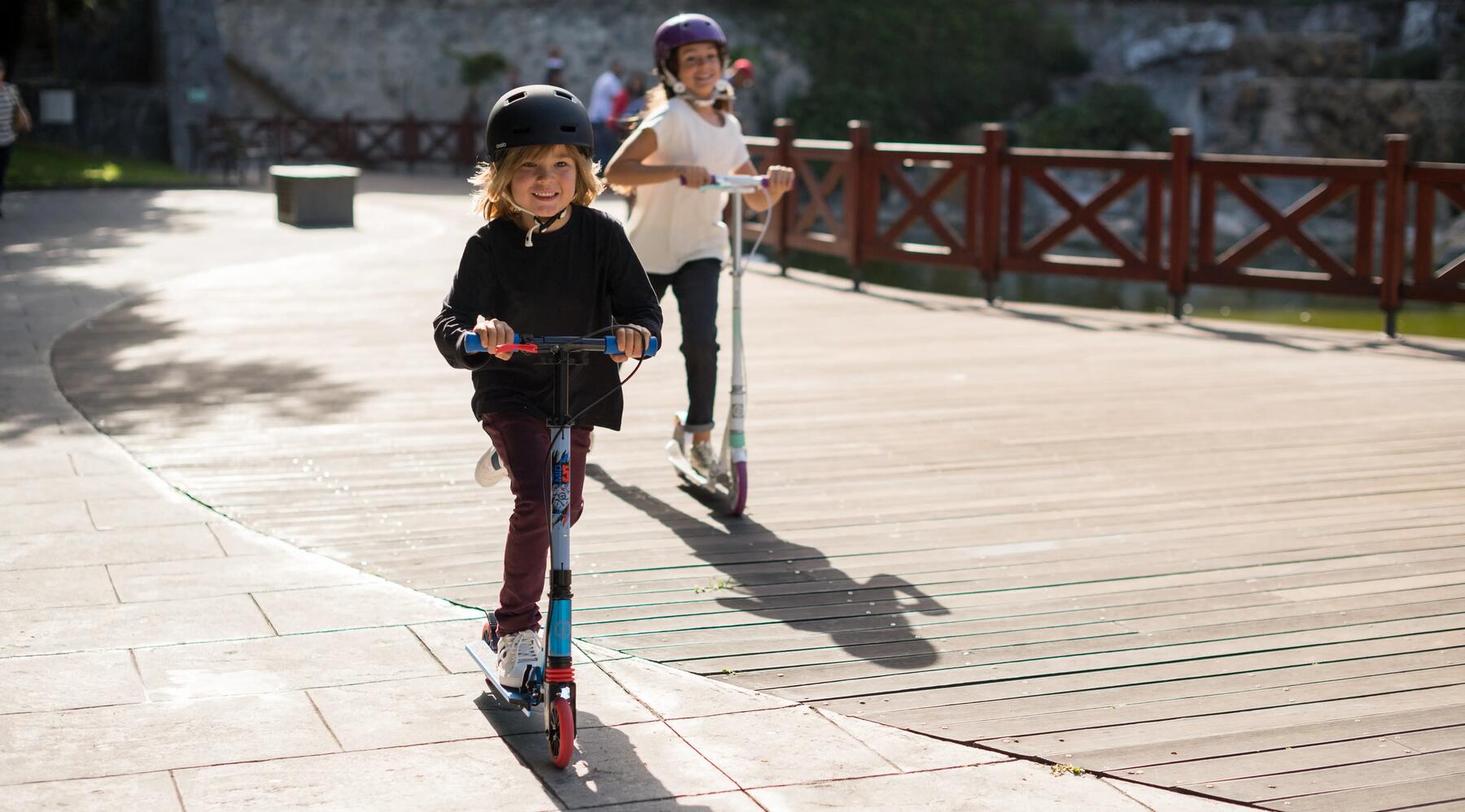 Zwei Kinder fahren mit einem Roller und tragen Schutzkleidung
