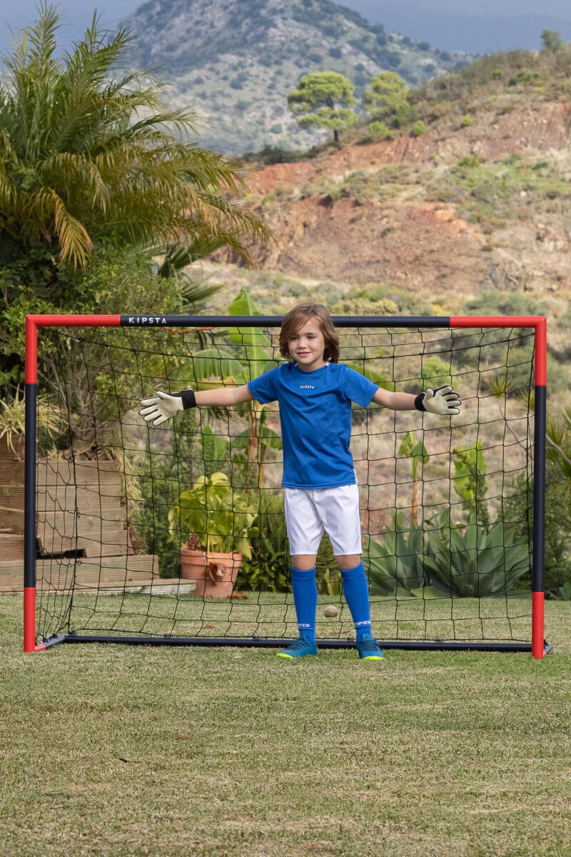 Malý fotbalista chytající v dresu a kraťasech ve fotbalové brance velikosti M.