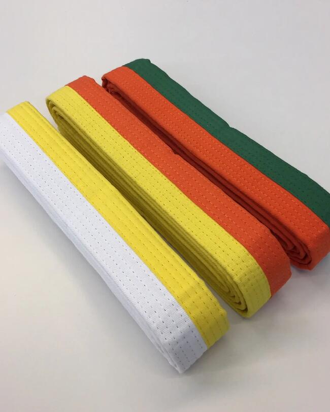 Zusammengelegte zweifarbige Kampfsportgürtel in Weiß-Gelb, Gelb-Orange und Orange-Grün auf weißem Untergrund.