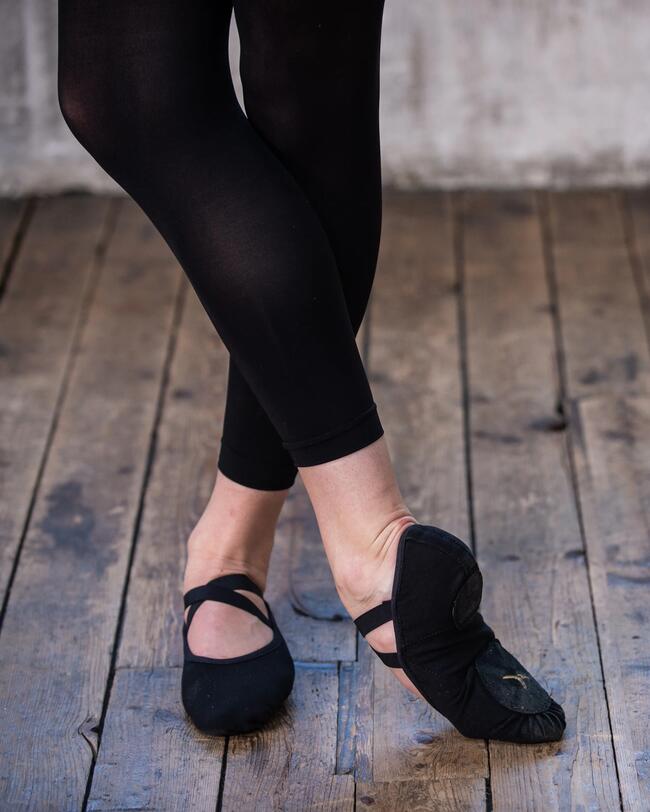 Eine Person trägt schwarze Ballettschuhe.
