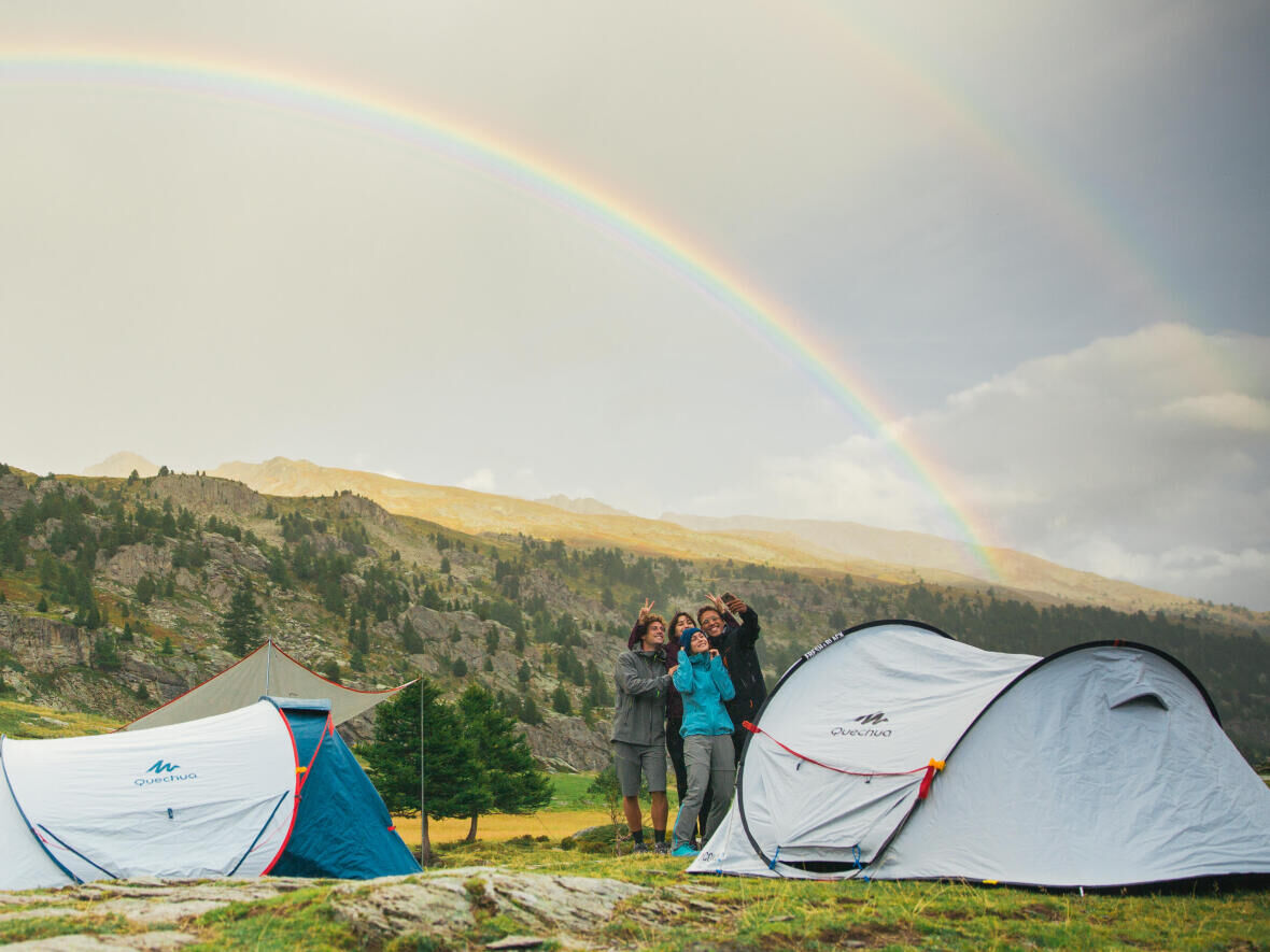 grupo de amigos a acampar na natureza com um arco íris 