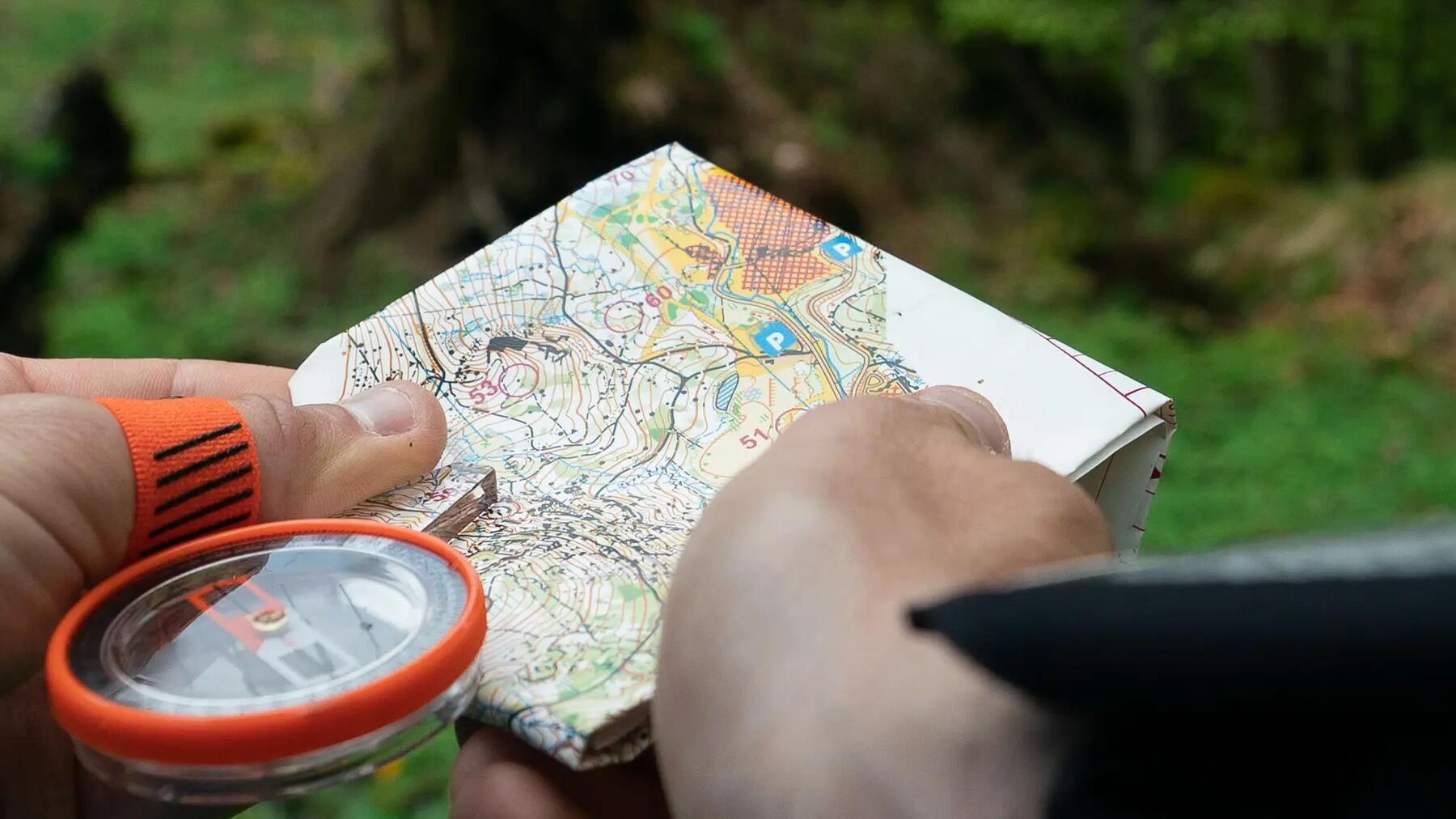 Geocacher im Wald löst Mystery Cache Rätsel mit Orientierungslauf Karte und Kompass