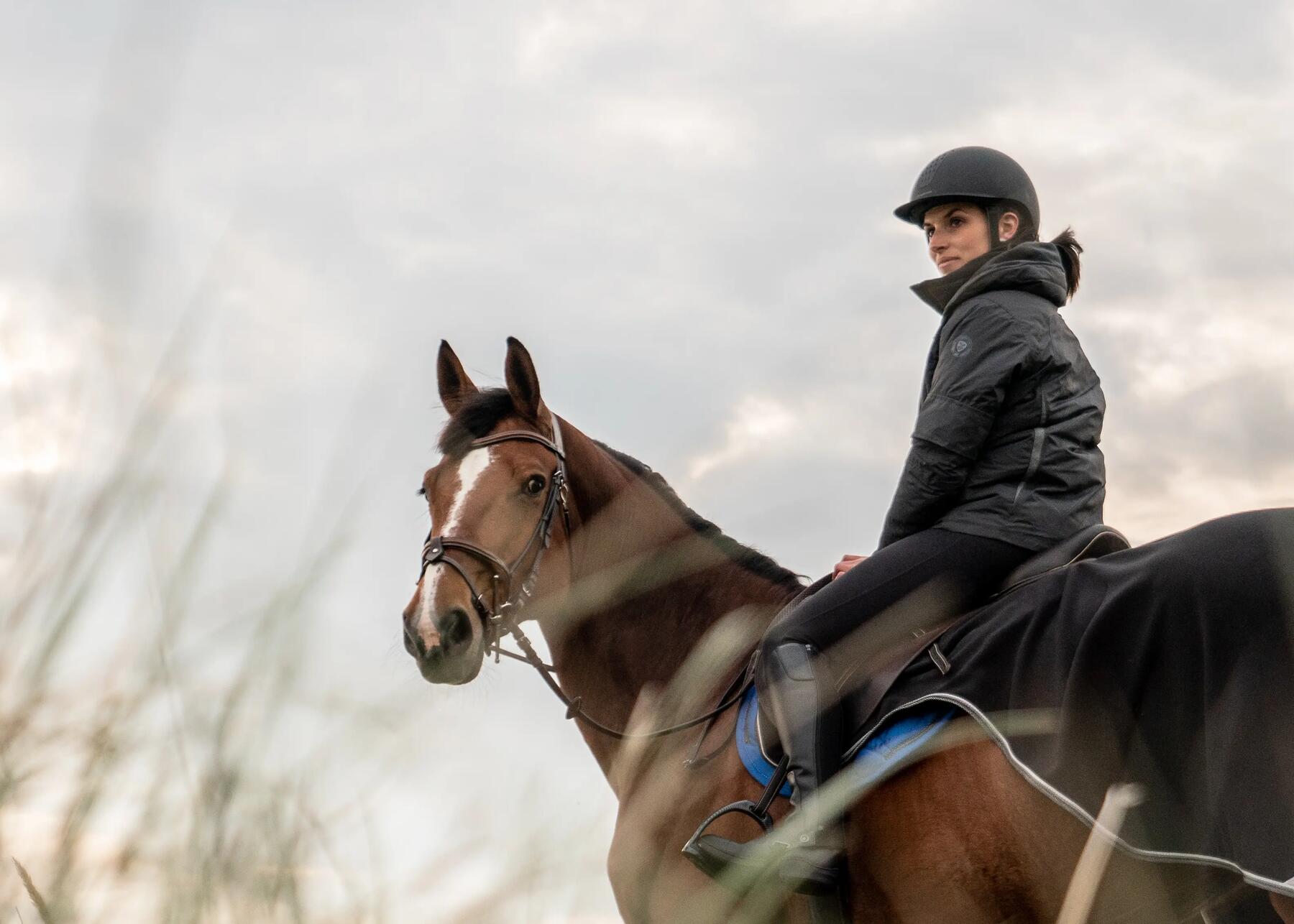 Cavaliere portant un casque, en balade avec son cheval entre les dunes d'une plage