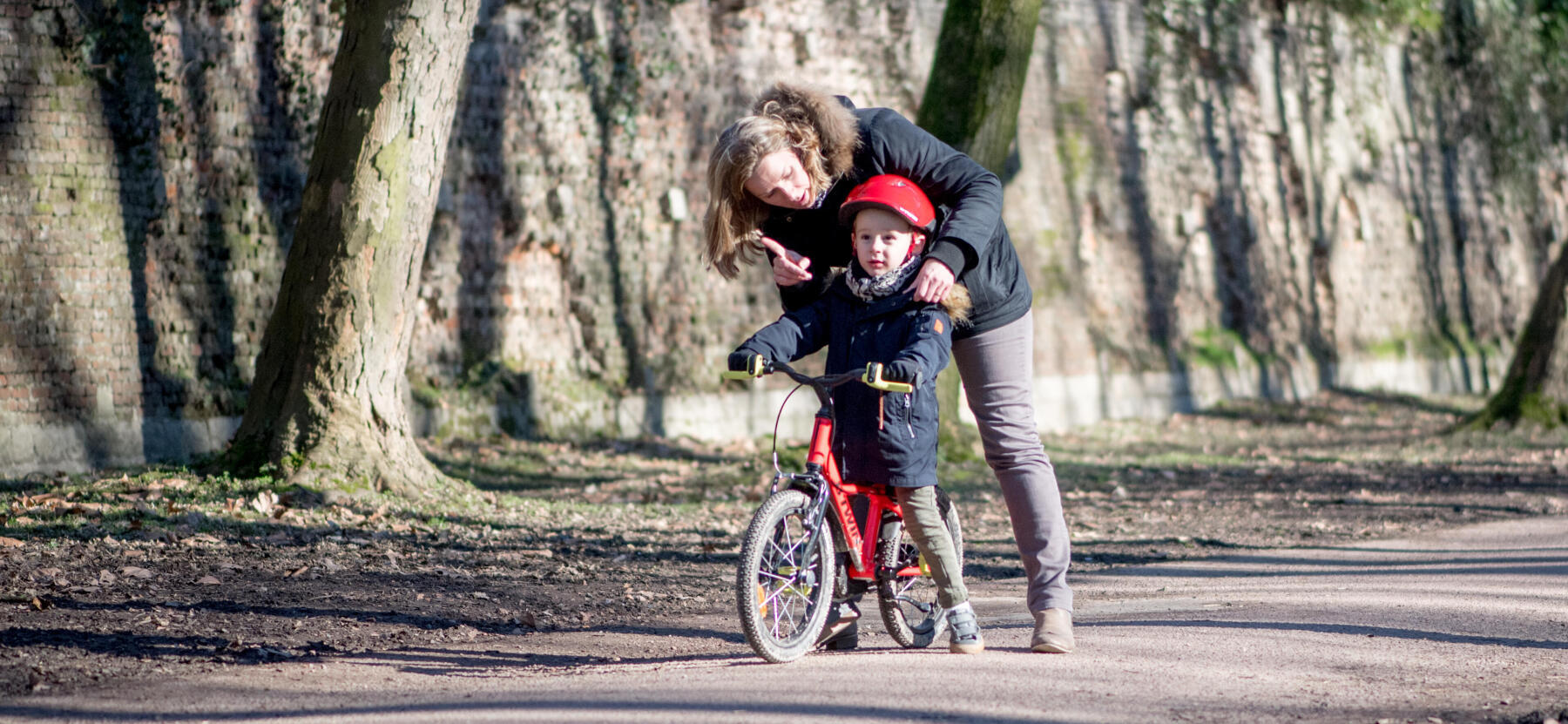 En kvinna står böjd över ett barn på cykel utan hjul