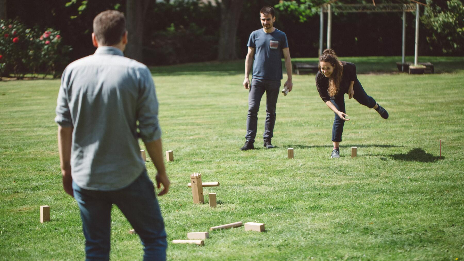 Drie mensen spelen kubb in een tuin