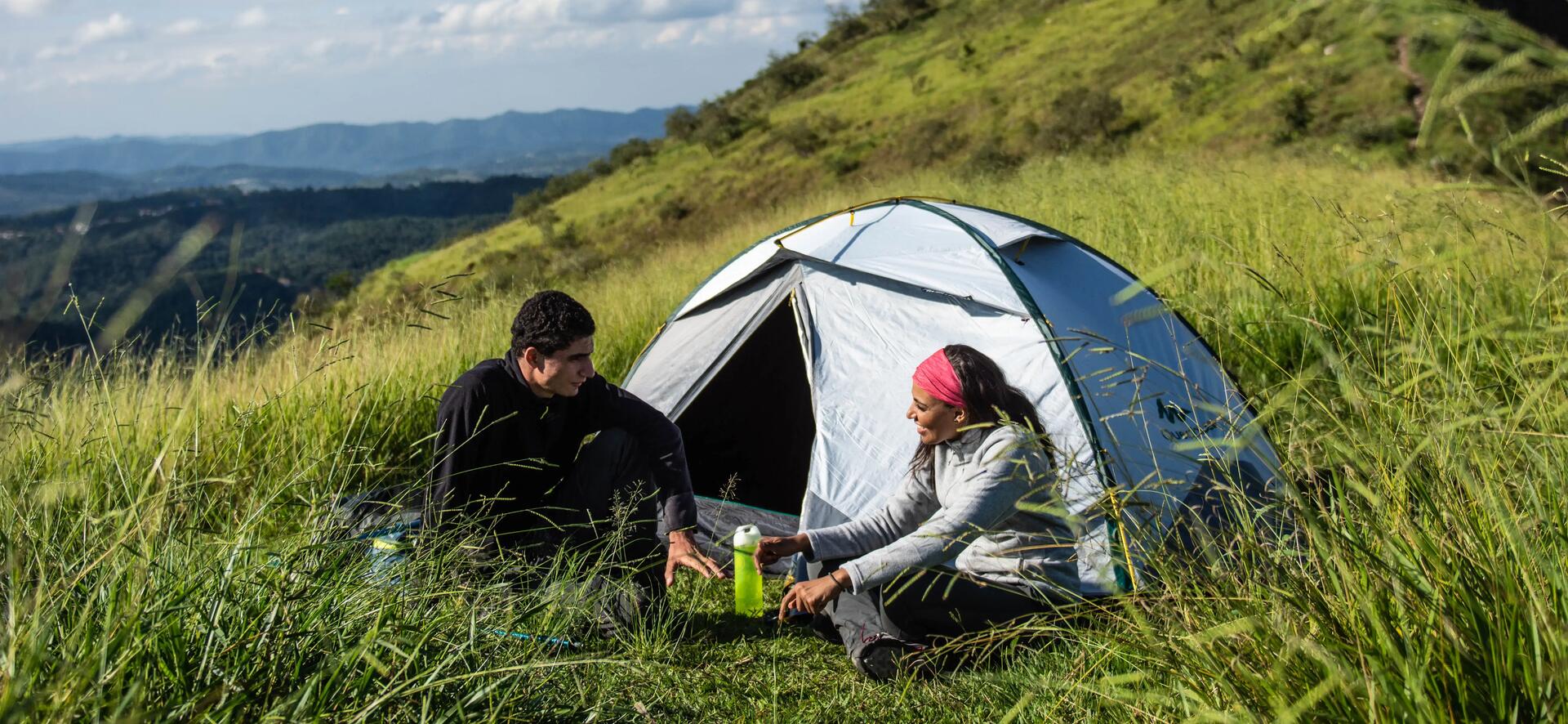 Zwei Personen sitzen vor einem Trekkingzelt im Gras