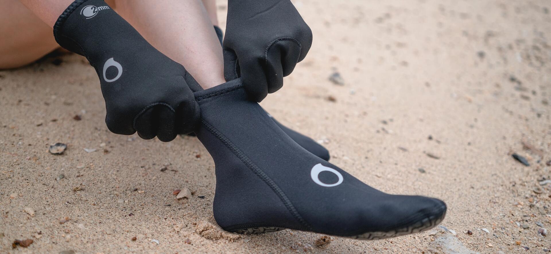 kobieta nakładająca buty neoprenowe na plaży