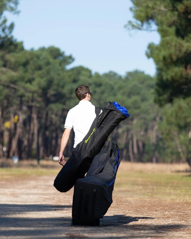 Mann in weißem T-Shirt, trägt große schwarze Tasche, läuft auf Waldweg, Bäume und blauer Himmel im Hintergrund.