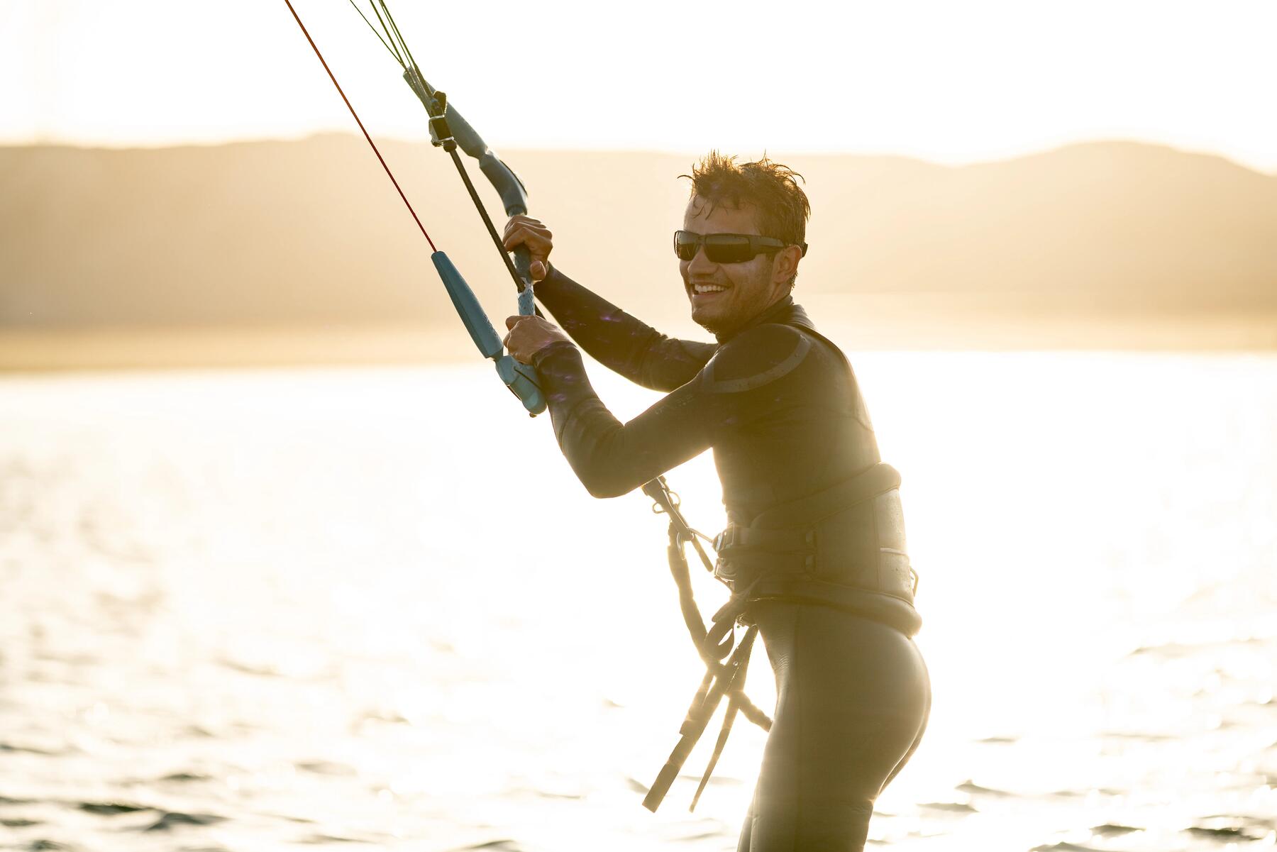 Mężczyzna w piance i okularach do kitesurfingu trzymający bar do kitesurfingu próbując utrzymać się na wodzie