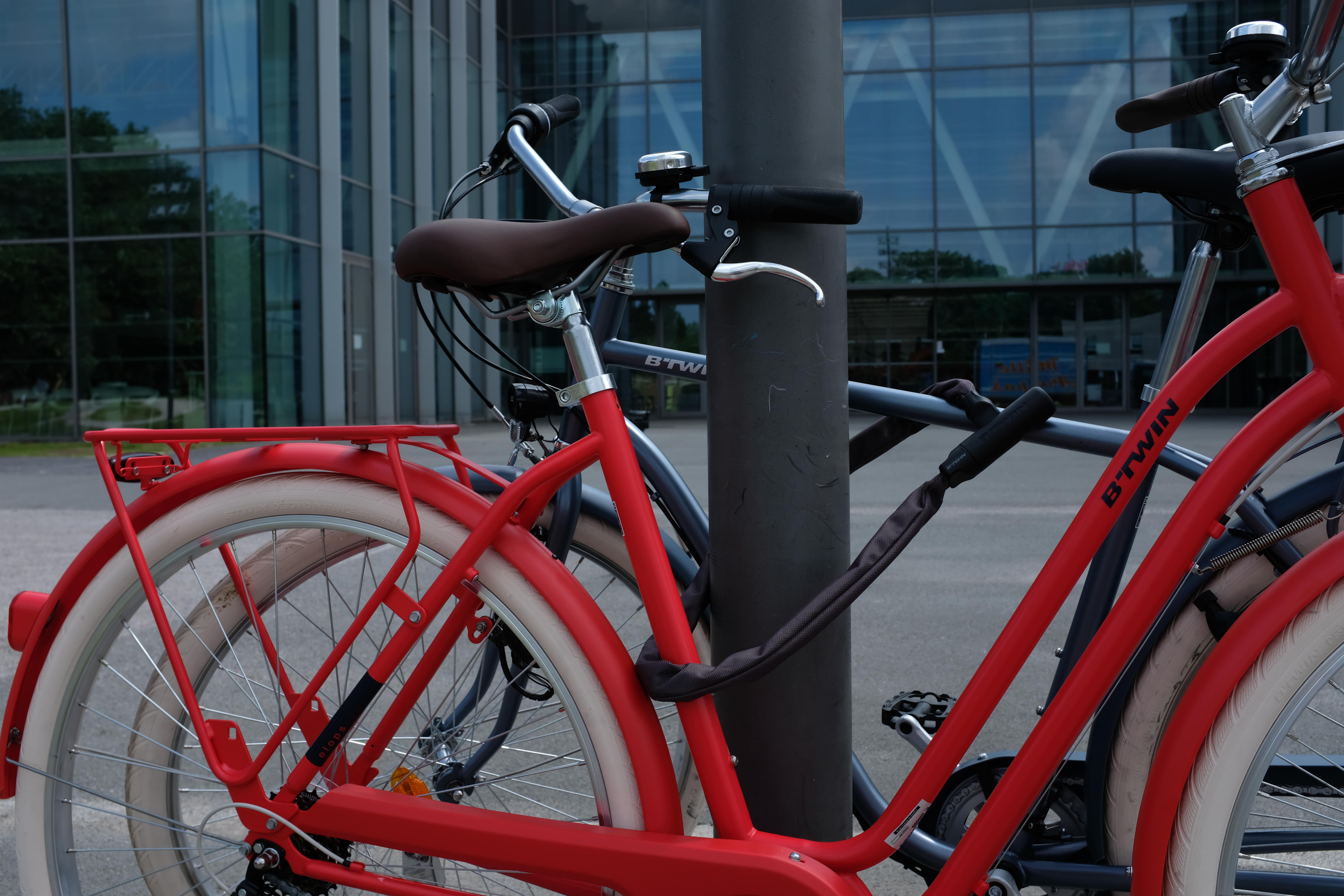 Two bicycles secured to a post with bike locks outside a building.