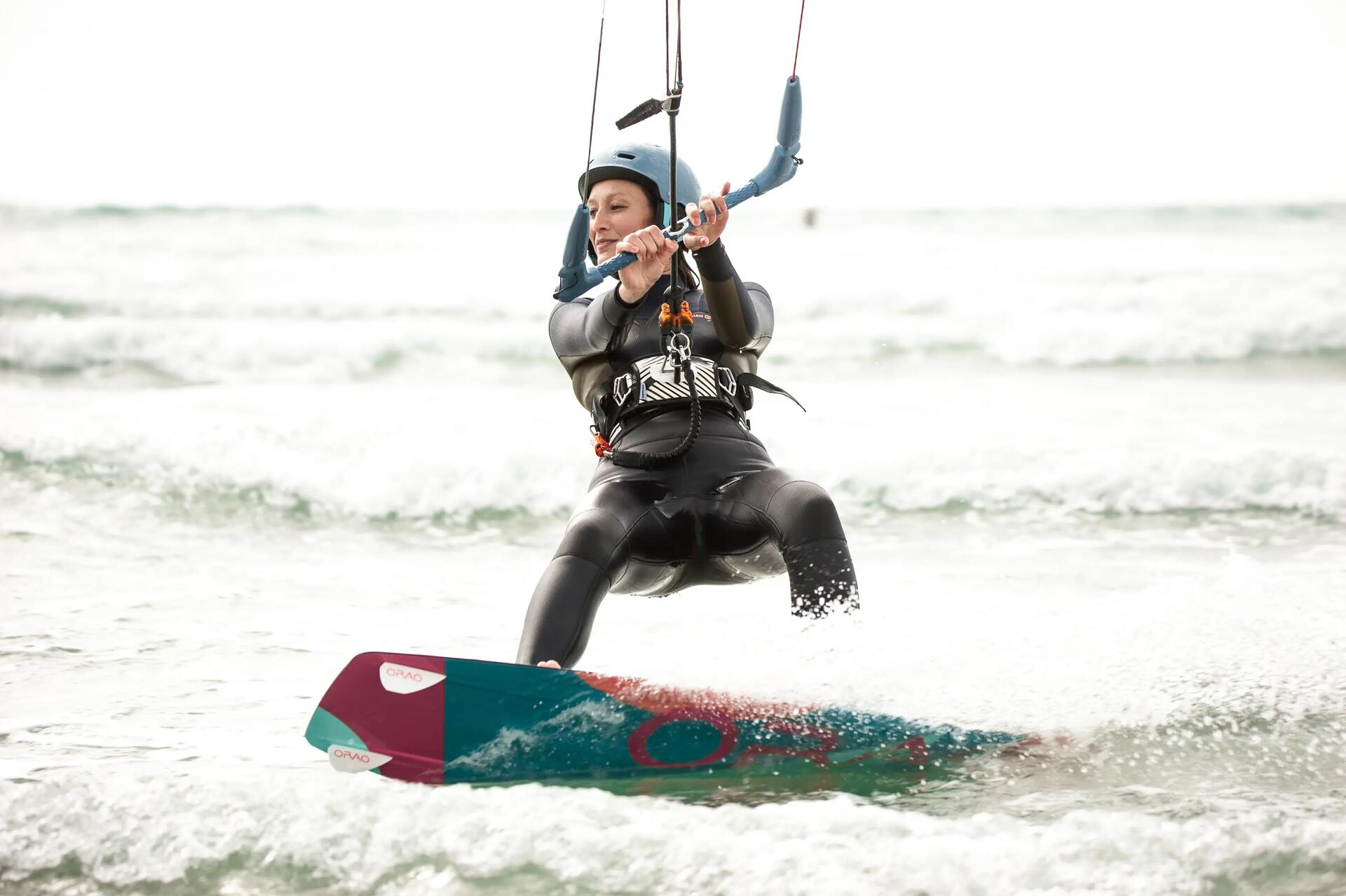Frontalansicht einer Kitesurferin im Neoprenanzug mit Steuerbar in den Händen