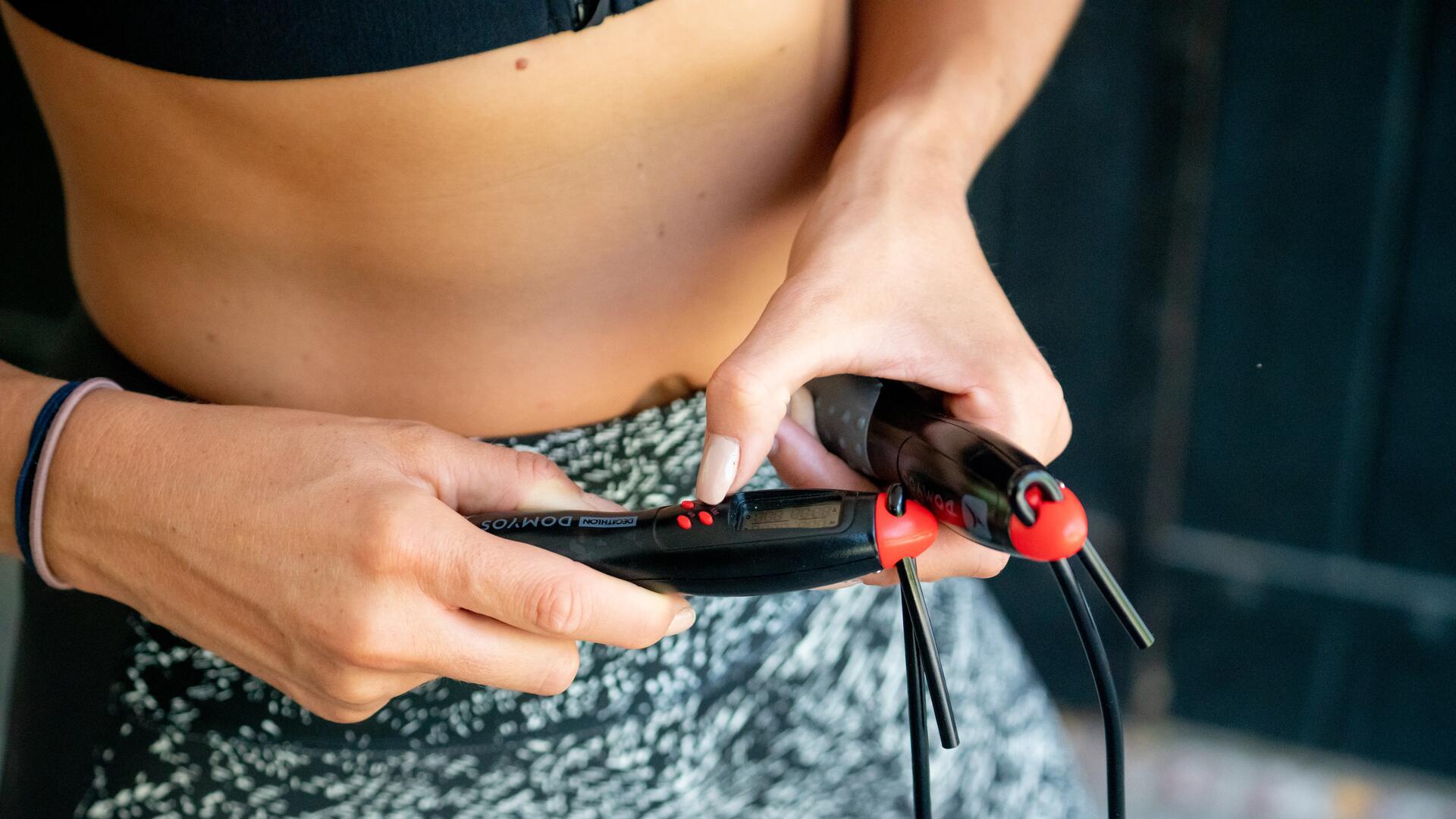 Kobieta w legginsach fitness trzymająca rączki skakanki z licznikiem