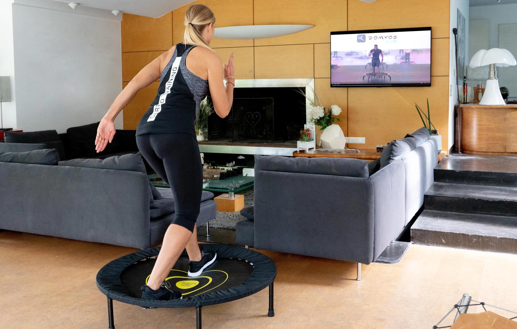 A woman using a mini trampoline in her living room watching a workout video on her TV