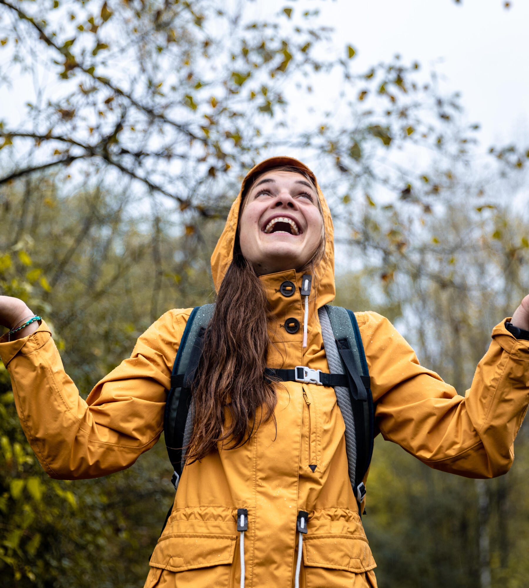 une femme souriante sous la pluie en randonnée avec son manteau jaune