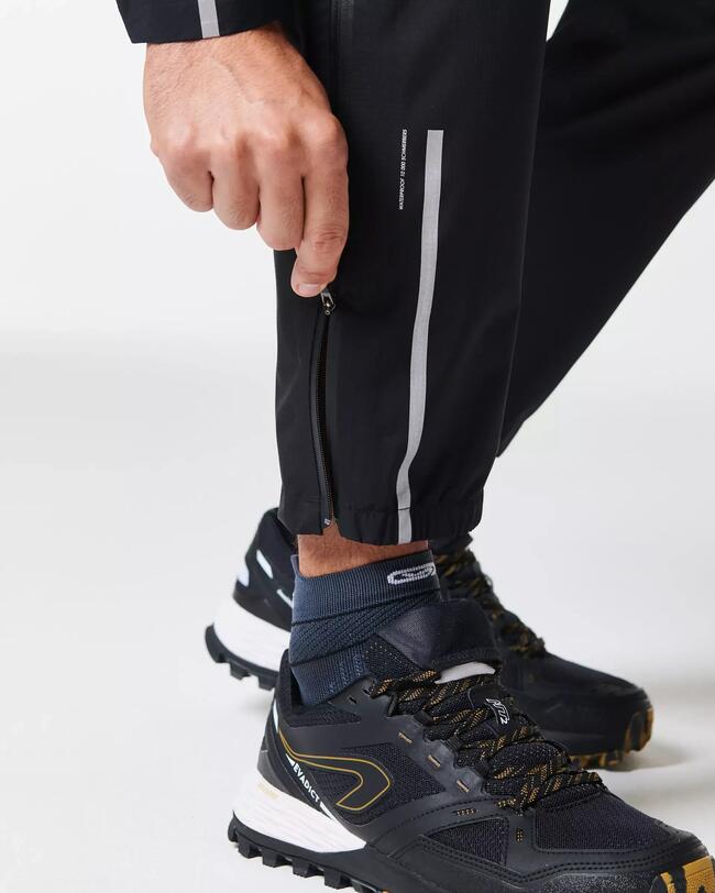 Hand zieht an schwarzem Reißverschluss einer Sporthose; schwarze und weiße Schuhe mit gelben Details.
