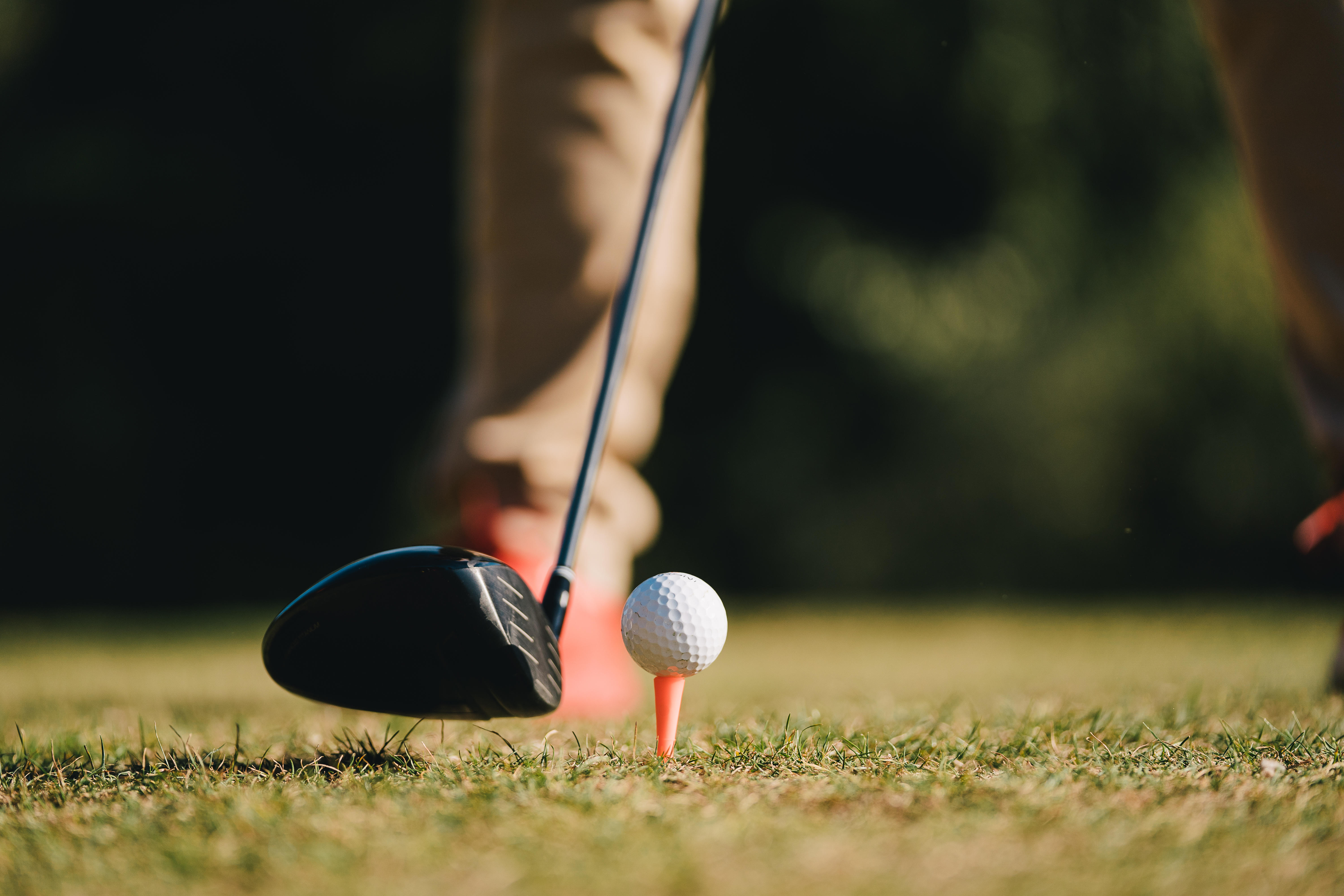 Golf club head resting behind ball on orange tee, close-up