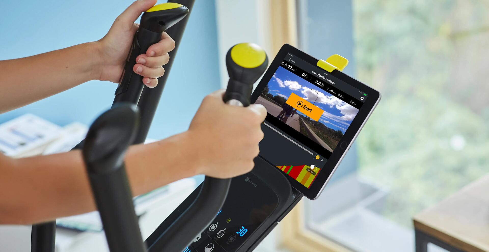 Rower eliptyczny z czujnikami do pomiaru tętna na kierownicy trzymany przez sportowca