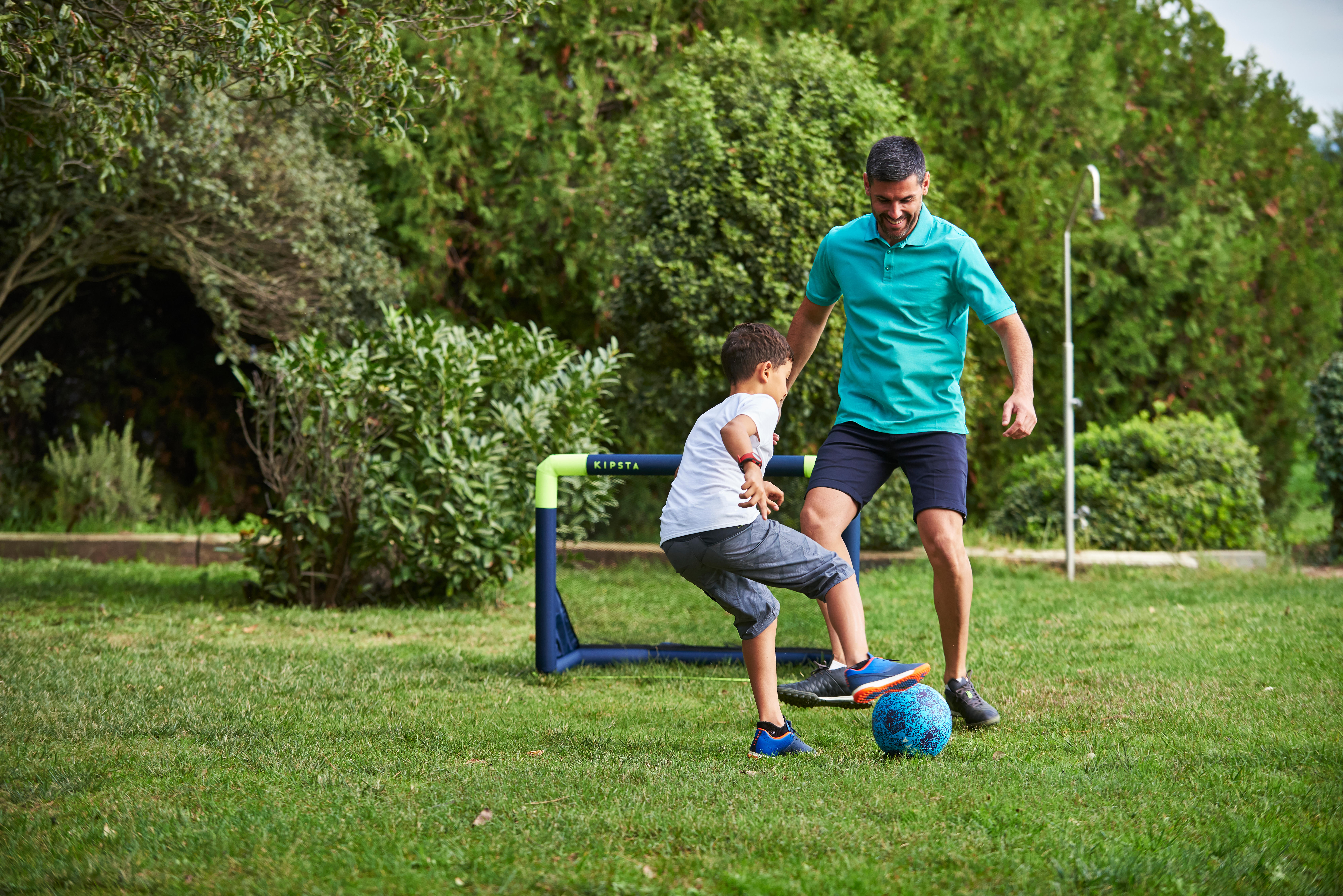 Man and boy playing football beside a small blue goal