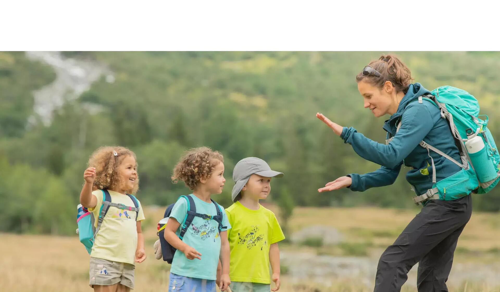 kobieta w odzieży trekkingowej z plecakiem na plecach bawiąca się z dziećmi