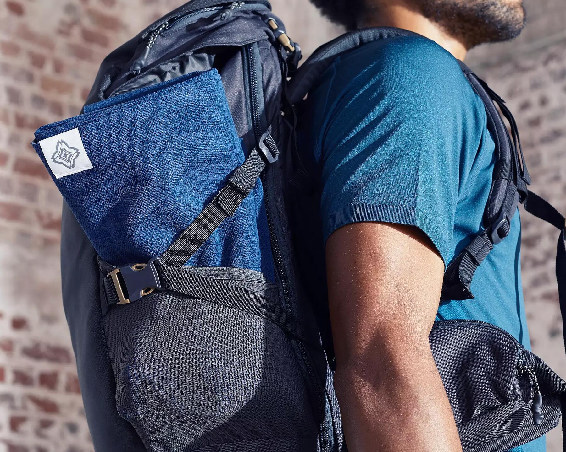 A man with a backpack and a Yoga Towel packed on the side of the backpack.